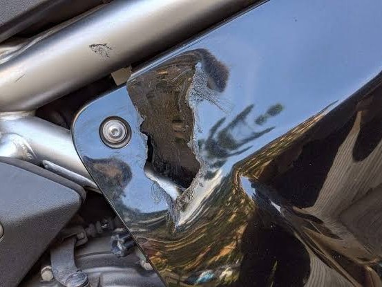 Black motorcycle side panel with a cracked, broken-out section